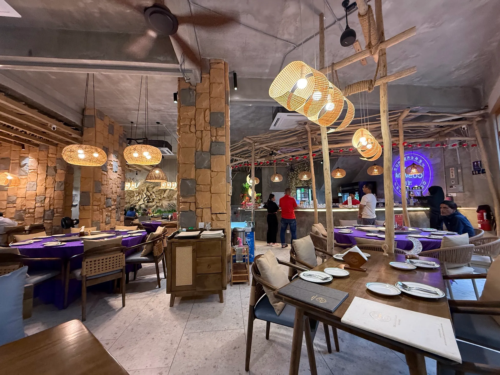 The main dining room with stone pillars, woven rattan pendant lamps and the restaurant's neon sign glowing over the bar