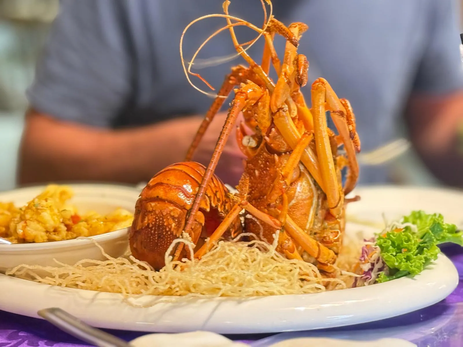 A whole lobster served upright on a nest of crispy fried vermicelli with salad